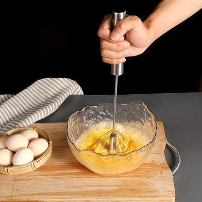 Hand using a hand mixer to beat eggs in a glass bowl on a wooden cutting board.