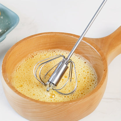 Wooden bowl with yellow mixture and metal whisk on a white background